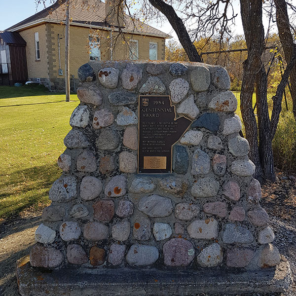 Hargrave Cairn and Hall. The stone cairn bears a bronze plaque in the shape of the province of Manitoba.